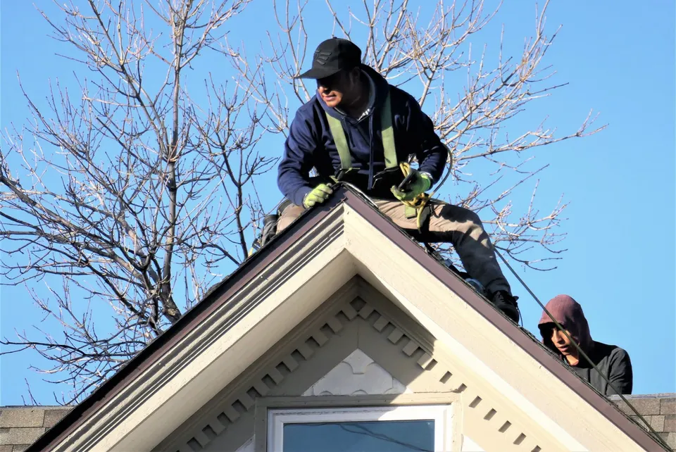 Two roofers working on the peak of a house roof